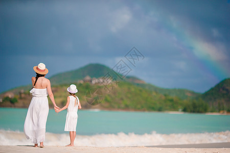 女士彩虹太阳帽年轻美丽的母亲和可爱的小女儿 在热带沙滩玩得开心 很快乐 加勒比人 异国情调背景