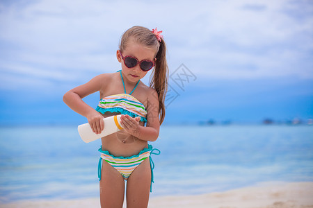 穿泳衣的可爱小女孩 拿着防晒霜水瓶子 棕褐色高清图片