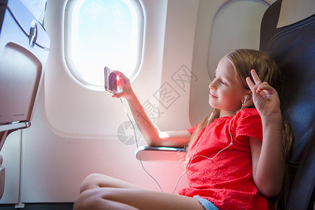 可爱的小女孩乘飞机旅行 坐在飞机窗边听音乐的孩子背景图片