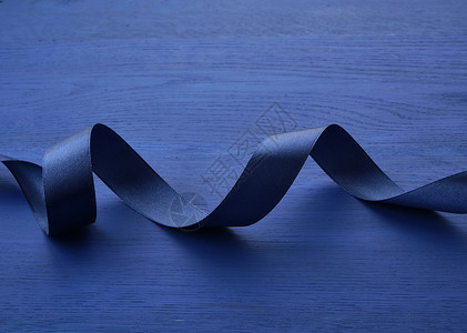 蓝色木质背景上缠绕的深蓝色丝绸细丝带背景图片