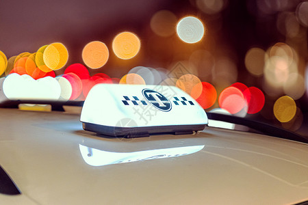 车顶上的计程车牌在市内交通灯光模糊 无重点的多彩照明下发光背景图片