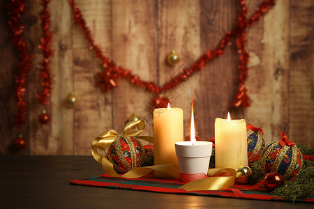 剪纸圣诞圣诞桌布上点着大火焰的蜡烛 周围有松树枝 剪纸小饰品 点燃的蜡烛和悬挂在木质背景上的圣诞装饰 具有散景效果 烛光 球背景