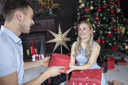 丈夫给妻子一份圣诞礼物 在圣诞树背景上情人们的情侣们 笑声  掌声 男性 美丽的背景图片