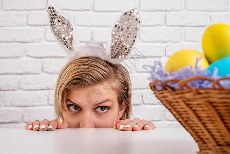 怀着兔子耳朵的女人看着篮子 带着复活节彩色鸡蛋图片