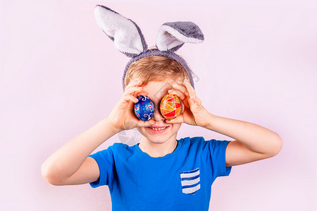 遮盖一只眼睛孩子白兔耳朵里的小可爱男孩头部闭上眼睛 用粉红背景的彩蛋闭着眼睛背景