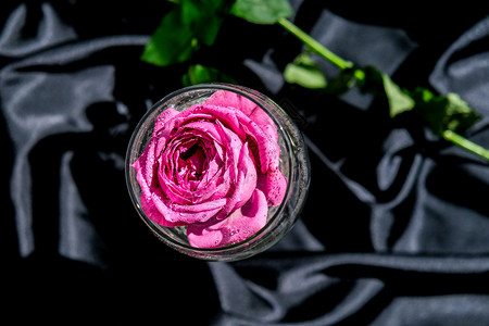装满粉红色花瓣的酒杯放在黑色丝织品的桌子上 最小的现代静物 假日概念情人节或女人节背景设计 小样 爱背景图片
