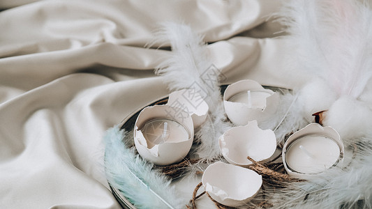 脱蛋壳衣服时髦的复活节装饰品 板上有裂纹的有机鸡蛋 鸡蛋白壳中的蜡烛 鸟羽 复制空间 问候卡 柔和的颜色 假期 复活节彩蛋背景