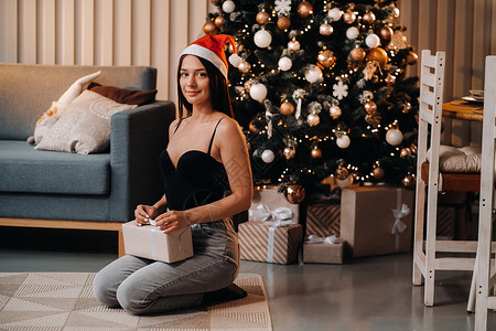 拿着新年礼物的女孩 坐在圣诞树旁边的家里 坐在家里呢! 女士背景图片