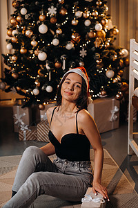 拿着新年礼物的女孩 坐在圣诞树旁边的家里 坐在家里呢! 黑发 盒子背景图片