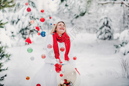 一个穿白色夹克的女孩扔圣诞球来装饰圣诞树 一个女孩把圣诞装饰品从篮子里扔进冬天的森林里 新年 花园背景图片