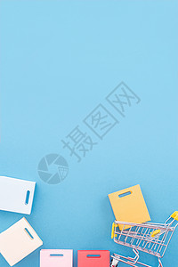 年度销售购物季的抽象设计元素概念-带纸袋的迷你黄色手推车 在柔和的蓝色背景顶视图平躺上隔离 展示 多于背景图片