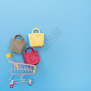 年度销售购物季的抽象设计元素概念-带纸袋的迷你黄色手推车 在柔和的蓝色背景顶视图平躺上隔离 蓝色的 展示背景图片