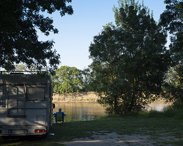男人坐在法国河堤岸边的露营车旁边高清图片