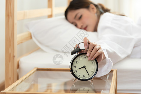 亚洲年轻美女早上很晚才关掉闹钟 不看钟 也懒得在假期工作 卧室和就寝时间概念 疲惫工人的放松和人们的生活方式 健康 女孩背景图片