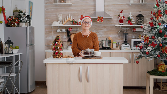 在装饰的厨房里庆祝圣诞节节 身戴圣诞帽的老女人的肖像 毛衣 饼干背景图片