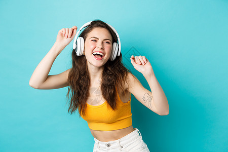 穿着夏装的年轻女性听音乐 戴着耳机 沿着最喜欢的歌曲唱歌 戴着耳机跳舞 站在蓝色背景下 假期 广告背景图片