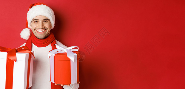 寒假 圣诞节和生活方式的概念 戴着圣诞帽和围巾的微笑帅哥的特写 祝新年快乐 拿着礼物 站在红色背景下的礼物 美丽的 毛衣背景图片