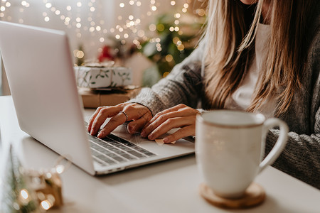 关闭妇女手 礼物 咖啡杯和膝上型计算机 圣诞节假期在线购物 从家庭办公室醒来的自由职业女孩 在笔记本电脑上打字的女性 圣诞时刻背景图片