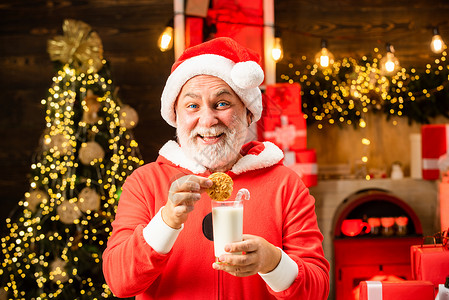 快乐的圣诞老人在家里的圣诞节室内吃着饼干 喝着一杯牛奶 圣诞老人喜欢在平安夜为他准备的饼干和牛奶背景图片