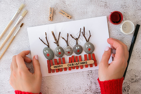 DIY贺卡贺卡明信片上的圣诞快乐鹿由鹅卵石 海石 衣夹和树枝制成 背景为白色 Diy 自然生态风格 diy 礼物的想法 一步步 顶视图 手背景