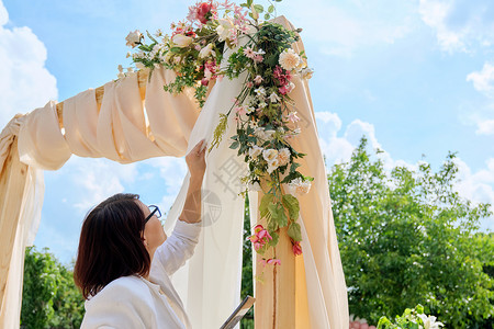 婚礼花卉拱门用带有花卉和植物的纺织品装饰拱门 女性组织者 所有者 在婚礼拱门附近有数字平板电脑 天 派对背景