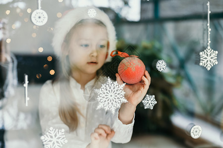 一个戴着圣塔克拉斯帽的女孩 看着窗户上的雪花 冬天背景图片