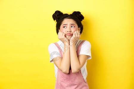 忧郁的亚洲女孩 双手瘦脸 面带愠怒的表情向左看 穿着黄色背景的夏装 美丽的 发型背景图片