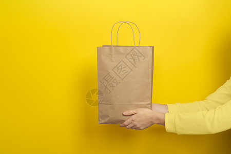 女性手拿着黄色背景的棕色手纸做的大礼品袋  可回收 假期背景图片