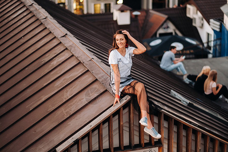 坐在屋顶上晚上 一个女孩坐在城里一所房子的屋顶上 穿着衣服和运动鞋的模特儿肖像 旅行 女士背景