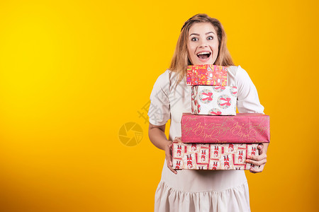一名穿着衣服 拿着礼物盒的开口大嘴巴快乐女孩的肖像 她们被黄色背景隔绝背景图片
