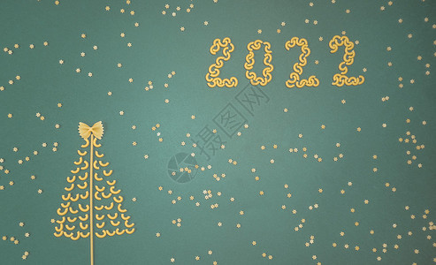 圣诞树上排列着干意大利面和数字 2022 绿纸背景上的星星来自意大利面 美食 健康背景图片