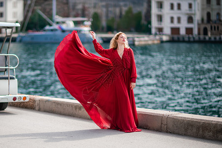 柳岩红裙飞舞身着红裙的女子 长着丝绸长翅膀的时装模特 身着飘逸的裙子 在堤岸上飞舞着布料 天空 挥手背景