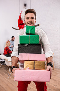 拍摄快乐的朋友享受假期 关注前景中戴着红色圣诞帽的礼盒的男人 庆祝背景图片