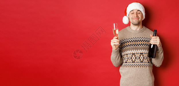 寒假 圣诞节和庆祝活动的概念 戴着圣诞帽和毛衣 在新年喝酒 拿着一瓶香槟和满满的玻璃杯 红色背景的快乐微笑男人的形象 瓶子 广告背景图片