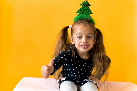 圣诞树2素材令人惊讶的快乐的小女学生圣诞树装饰 头领圆点服装展示橙色背景的拇指 新年 节日 庆典 冬季概念等都值得一提 黄色 胡萝卜背景