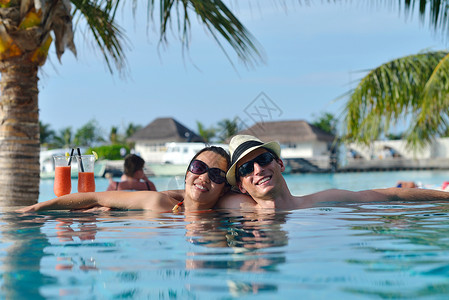快乐的年轻夫妇放松 在游泳池边喝新鲜饮料 海 棕榈背景图片