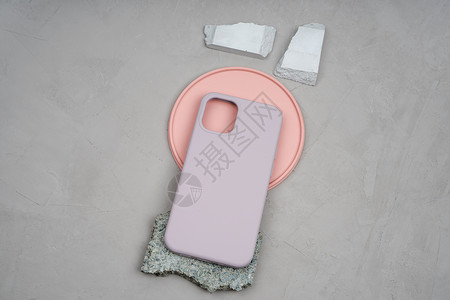 米色智能手机硅胶保护套 智能手机的外壳放在一块珊瑚色的圆形石膏板上背景图片
