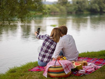 电话银行夫妻在享受野餐时间时用手机拍自拍 女朋友 夏天背景