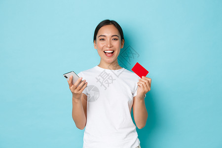 电子商务 购物和生活方式的概念 满意的成功亚洲女孩拿着智能手机和信用卡欢欣鼓舞 在网站上打折 在网上购物背景图片