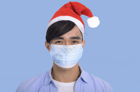 戴着圣诞帽子和面罩的年轻人 为了安全免受 Corona病毒共感染19 男人 圣诞老人背景图片