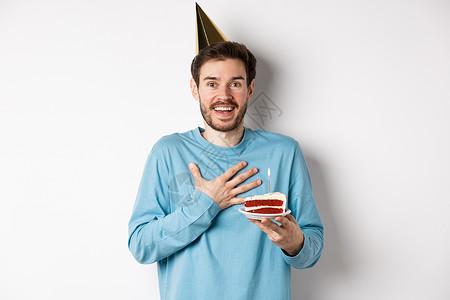 庆祝活动和假期的概念 惊讶的生日男孩戴着派对帽 拿着生日蛋糕 看起来很感激 站在白色背景上 快乐的 脸背景图片