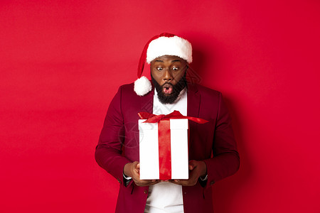 圣诞 新年和购物概念 令人惊讶的黑人在看Xmas礼物 说哇哇啊 收到假日礼物 红背景 成人 商业背景