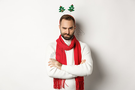圣诞晚会和庆祝活动的概念 可疑的留着胡子的年轻男子看起来很可疑 戴着滑稽的配饰帽 站在白色背景下背景图片