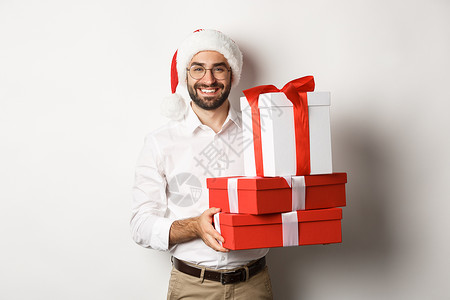圣诞快乐 假期概念 快乐的年轻人微笑着 拿着盒子里的礼物 戴着圣诞帽 白色背景 黑发 庆典背景图片