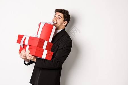圣诞假期 庆祝活动和生活方式的概念 穿着黑色西装的帅哥 拿着一堆礼物 微笑着 祝新年快乐 站在白色背景上 快乐的 幸福背景图片