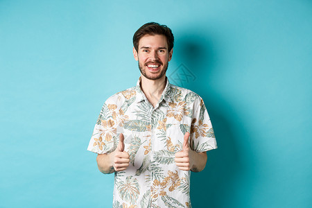欢乐的旅游者露出认可和微笑的拇拇指 穿着hawaiian衬衫 推荐旅行社 蓝底背景 胡须 生活背景图片