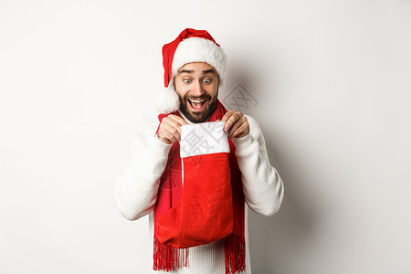 冬季假期和庆祝活动的概念 快乐的人看着圣诞袜 收到新年礼物 站在白色背景上 购物 工作室背景图片