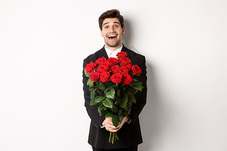 穿着黑色西装的英俊男友的形象 手捧红玫瑰花束 微笑着 正在约会 站在白色背景上 订婚 男性背景图片