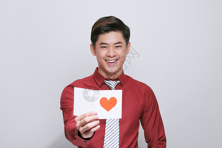 亚裔男子持有情人节日卡 有心胸 孤立在白色上背景图片