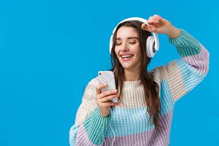 耳机促销x展架快乐的魅力和无忧无虑的微笑欧洲女性在作为圣诞礼物收到的新耳机中享受美妙的音乐质量声音 举起手拿着智能手机 蓝色背景背景